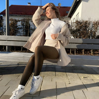 Woman wearing Formivelle fleece-lined tights, white jacket and sneakers, sitting on bench outdoors