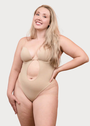 Smiling woman wearing a nude Formivelle backless thong bodysuit, front view, on plain background.