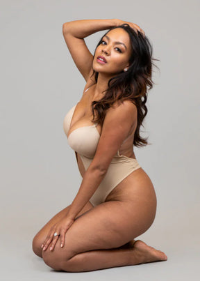 Woman modeling a beige Formivelle backless thong bodysuit on a neutral background.