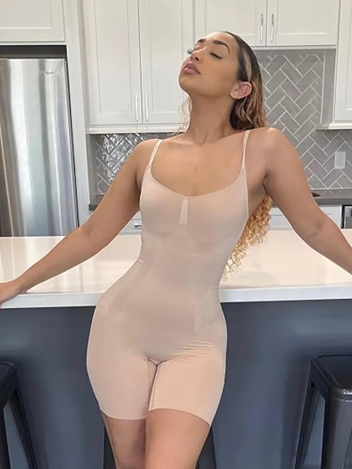 Woman wearing Formivelle nude mid-thigh bodysuit shapewear in a modern kitchen